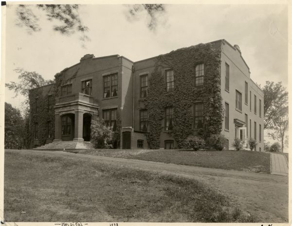 Exterior view of front entrance of the Hospital building at The Northern Wisconsin Colony and Training School. Climbing vines cover the exterior wall of the building.
