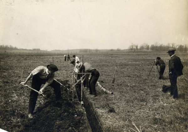 View of a crew surveying land, digging a ditch, and laying drain tile.