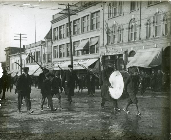 Men carrying skis march behind a drummer down Main Street.