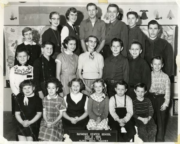 Group portrait of first through eighth grade students at Raymond Center School with their teacher, Gloria Bicha. One boy wears a Davy Crockett shirt.
