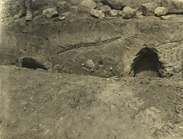 Excavation site of two graves discovered on Bascom Hill during preparation for placement of the Abraham Lincoln monument circle. The legs and shoes of a man standing on  the edge of the grave site is on the left. The hill was the site of the first cemetery in Madison.