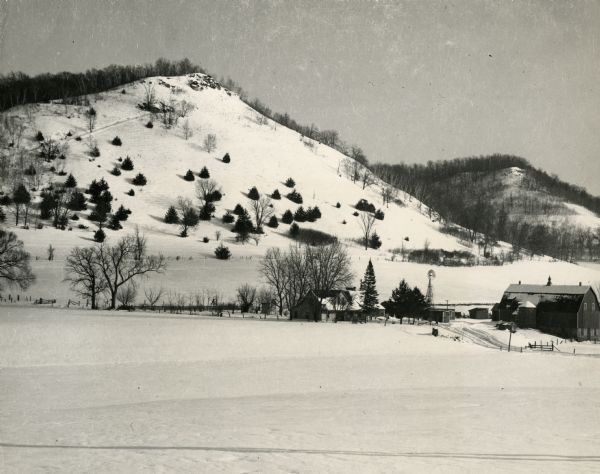Winter scene of a snow-covered hillside with a farm below.