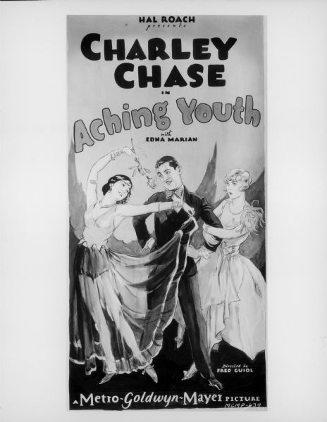 Photograph of a poster for the 1928 film <i>Aching Youth</i> starring Charley Chase. Chase stands at the center of the poster with his hands on his hips. He looks at a woman holding a flower over her head while another woman holds on to his arm.