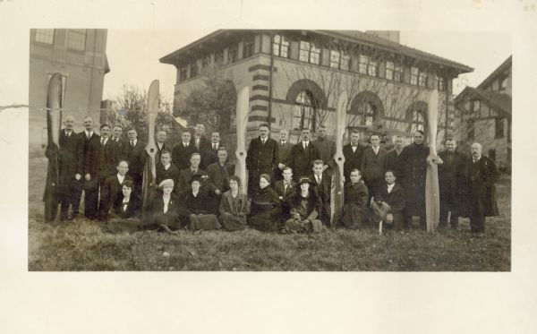 Group of men and women from Forest Products Lab posed with wooden propellers in front of a building.