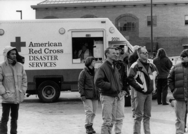 View towards a small group of people watching as fire destroys the Hotel Washington. Behind them is an American Red Cross disaster services vehicle.