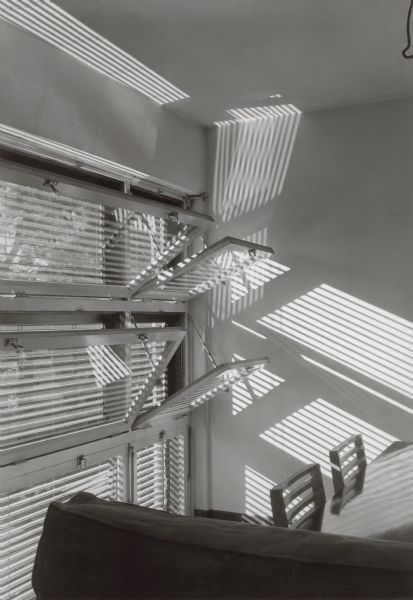 Interior view of the windows designed for the Keck-Gottschalk apartment building. The windows are angled open and the sun is shining through the exterior Venetian blinds.