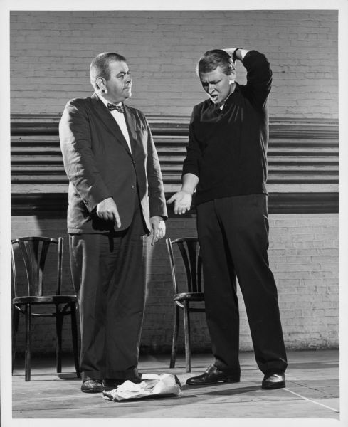 Publicity photograph for the 1962 play "A Matter of Position." Mike Nichols has a confused look on his face and points at something on the floor. Rex Everhart points to the object on the floor and gives Nichols a stern look.