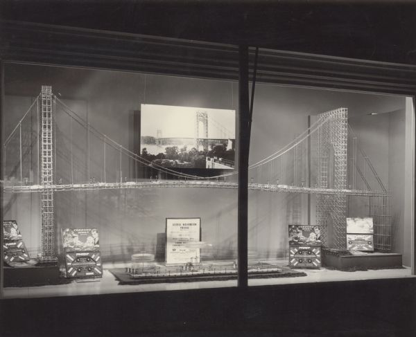 Window display of a toy "George Washington Bridge" constructed from Cozzone Construction Sets. Cozzone Construction Set boxes and parts are also displayed. A text panel in the display states that the bridge model was constructed from "Carrom Cozzone Construction Sets," as at the time, Cozzone sets were being sold by Carrom Industries.