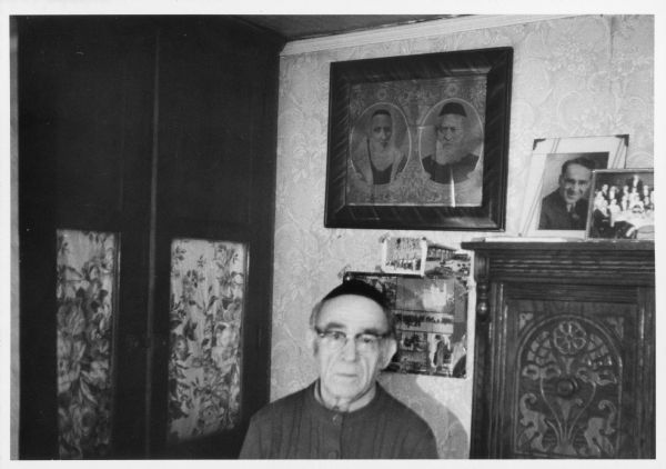 Rabbi Alex Hyatt stands in front of framed photographs displayed on the wall.