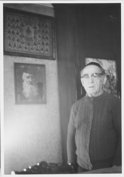 Rabbi Alex Hyatt poses next to an framed portrait of a man with a white beard who is possibly also a rabbi.