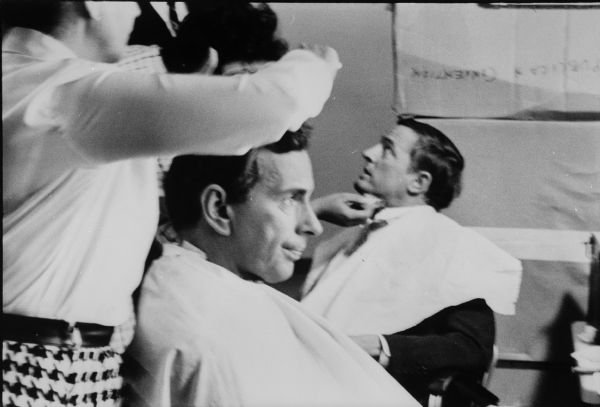 Gore Vidal (left) and William F. Buckley (right) each sit in a chair while they have makeup applied before a television appearance.