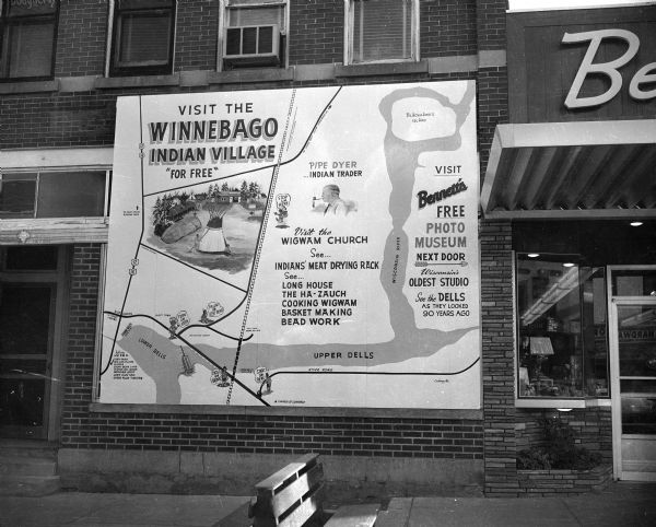 View from street of a sign hanging at 211 Broadway, advertising the Winnebago Indian Village, which was managed by Pipe Dyer.