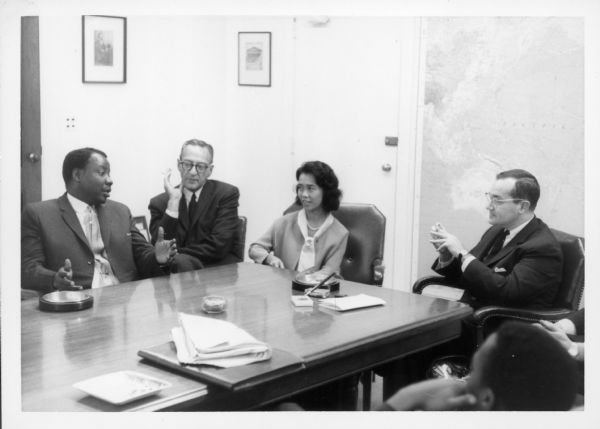 Newton Minow (far right) is seated at a table with members of his staff at the Communications Research Center. There is a large map on the wall on the right.