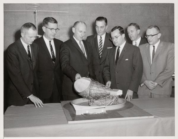 A group of men look at a model of the Telstar with Newton Minow.