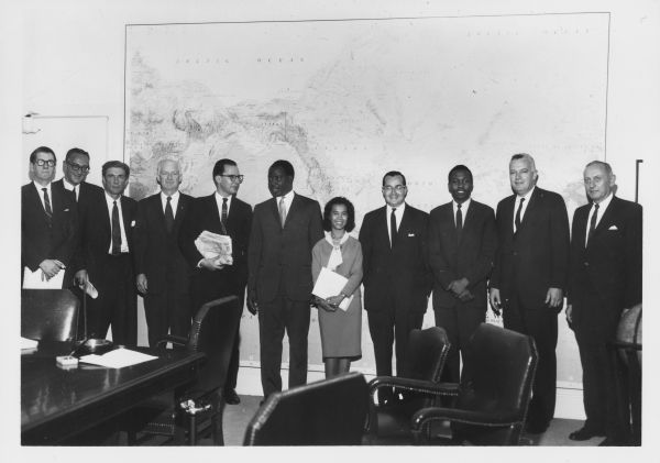 Newton Minow (fourth from the right) poses with members of his staff in front of a large map on a wall.