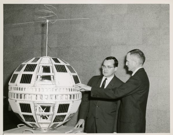 Newton Minow and another man look at a model of the Telstar satellite.
