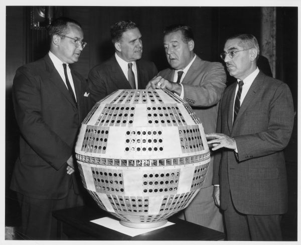 A group of men study a model of the Telstar satellite. From left to right are: Newton Minow, chairman of the Federal Communications Commission, James Webb of National Aeronautics and Space Administration, Warren Magnuson, chairman of the Senate Commerce Committee, and Senator John Pastore of the Communications Subcommittee.