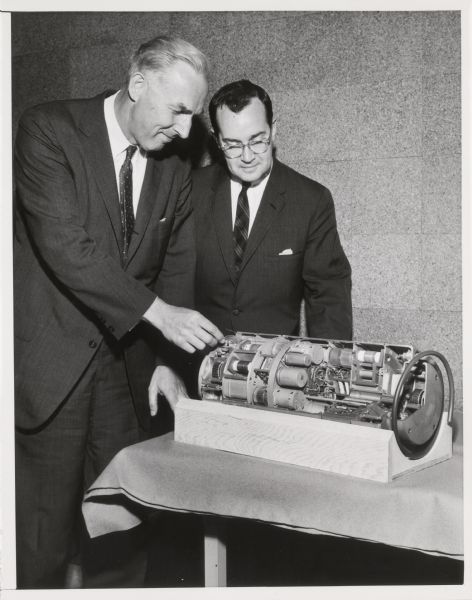 Newton Minow (right) and another man inspect what may be a communications part.
