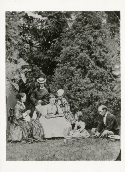 Formal outdoor family group portrait. From left to right are Delia Scott Fowler (who is knitting), Caroline Fowler Gilbert (standing), Gertrude Fowler (seated in front of Caroline), Della Gilbert, Carrie Tucker (seated on the grass), and Dr. C.B. Gilbert, who is sitting on the grass holding a croquet mallet.