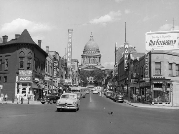 View up State Street towards the Wisconsin State Capitol taken from the West Johnson Street intersection. Businesses include the Orpheum Theatre, Arenz, and Ward's. There is a billboard for Old Fitzgerald Kentucky bourbon on the roof on the right.