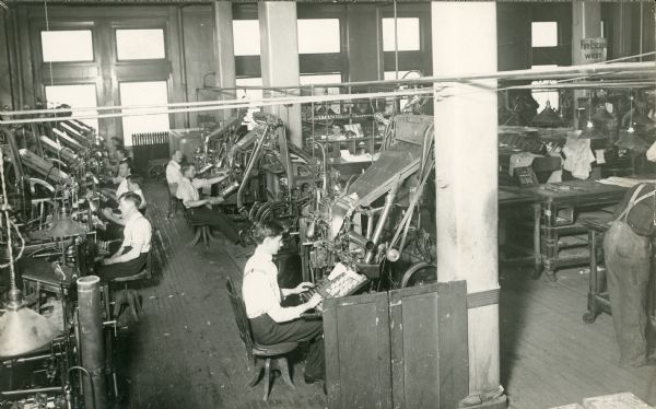 Slightly elevated view of several men are seated in the composing room of the <i>Milwaukee Sentinel</i>, setting type for the newspaper.