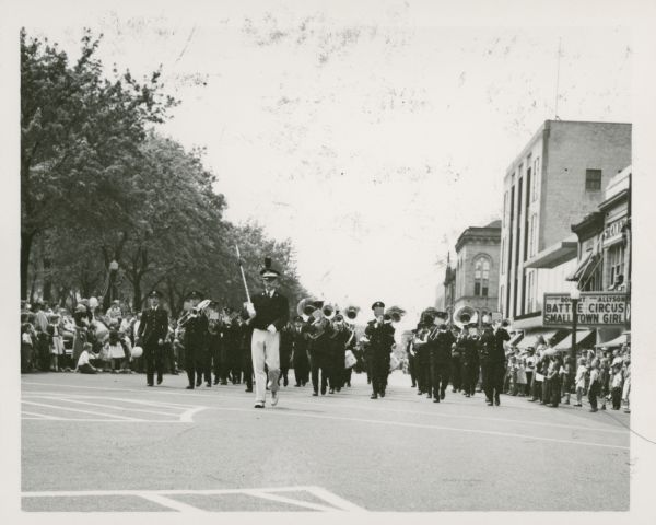View from street of the University of Wisconsin Marching Band parading down Mifflin Street, past the Strand Theater. This parade took place on Armed Forces Day.