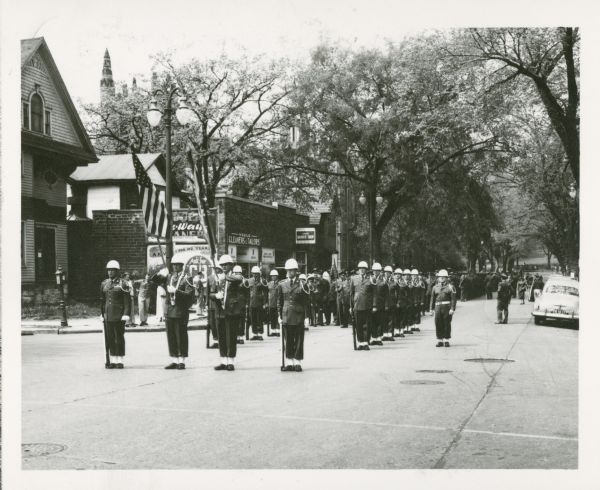 View down the 700 block of State Street towards the Truax Field Honor Guard marching past the State Barber Shop on Armed Forces Day. Park Street and the bottom of Bascom Hill are in the background.