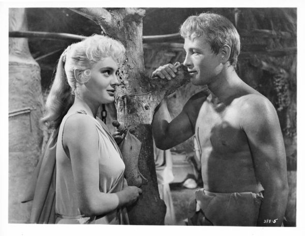Still of Rossana Podesta as Helen and Jacques Sernas as Paris from the 1956 film "Helen of Troy." The two gaze into each others eyes as they stand opposite each other.