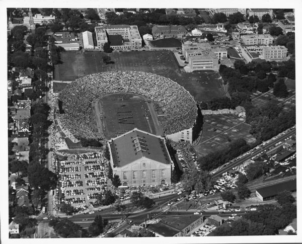 Aerial view of a full Camp Randall Stadium during half-time of a football game. The band is on the field in formation to spell "UW."