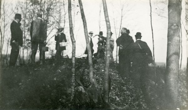 A field party of members of the Wisconsin Archaeological Society visit an effigy mound at Big Bend. The men are dressed in suits and hats.