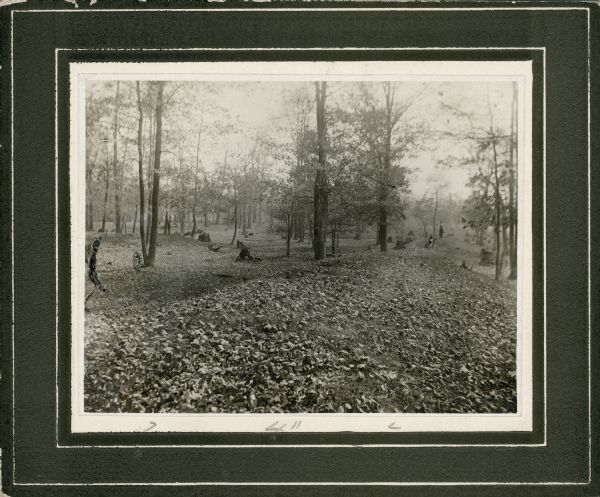 View of a linear Indian mound at Big Bend. Two men stand in the background on the left and right among the trees.