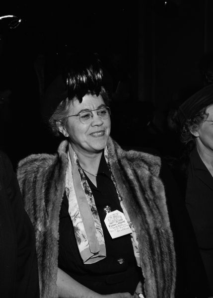 Mrs. J.D. Hahlen of Brodhead, Wisconsin attends an event for the University of Wisconsin Farm & Home Week on the Madison campus. She is wearing a fur coat and a hat with feathers.