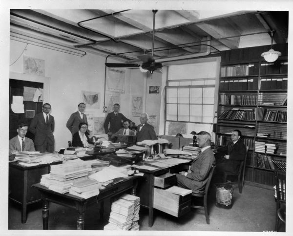 Staff members at the University of Wisconsin-Madison Institute For Research in Land Economics and Public Utilities sit together in a room in Sterling Hall. From left to right are Herbert Doran, Herbert Simpson, Richard T. Ely, George Wehrwein, William Haken, Mary L. Shine (later Mary Peterson), David Rozman and Edward W. Morehouse.