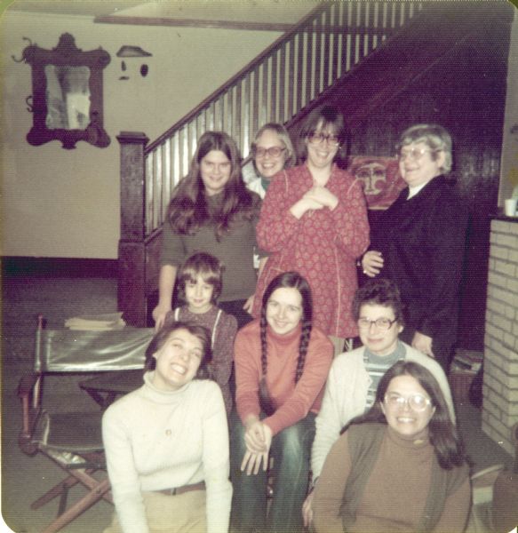 Group portrait of attendees of the organizing meeting of the Wisconsin Women Library Workers. The meeting appears to be in someone's home. From left to right in the front row are: Meg Wise and Donna Barkman. From left to right in the middle row are: Heather Leide, Kathy Leide and Carolyn Wilson. Standing in the back from left to right are: Robin Barkman, Grethe Jacobsen, Kathy Weibel and Margaret Myers.