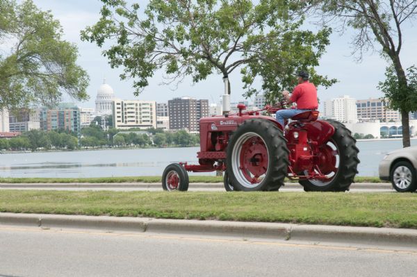 A man drives a tractor on John Nolen Drive along Lake Mendota with the Wisconsin State Capitol in the distance. He is on his was to a Red Power venue held at the UW libarry mall in front of the Wisconsin Historical Society.