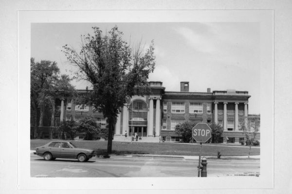 Exterior view from across street of Atwater School at 2100 North Capitol Drive. There are several people on the school front steps. A car is driving on the left, and a stop sign is in the foreground.