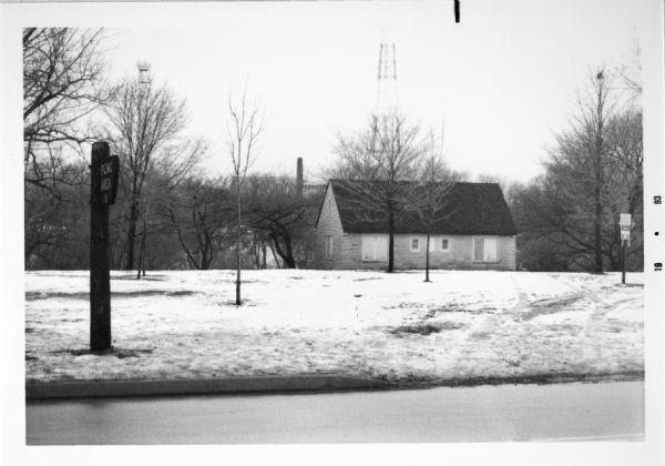 View across street towards snow-covered Estabrook Park, including a side-gabled building.