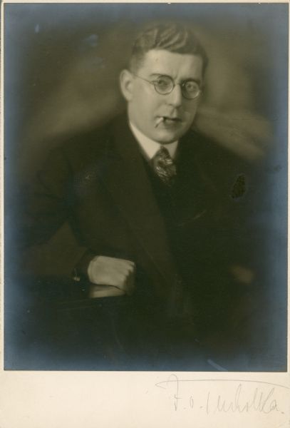 Waist-up seated portrait of Leo Lania (born Lazar Herrmann) resting his arm on a table and smoking a cigarette.