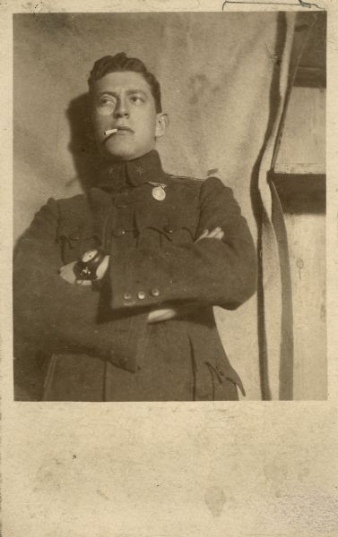 Waist-up portrait of young Leo Lania (born Lazar Herrmann) posing in a military uniform with his arms folded. He is wearing a monocle, and what may be a large watch or compass on his wrist.