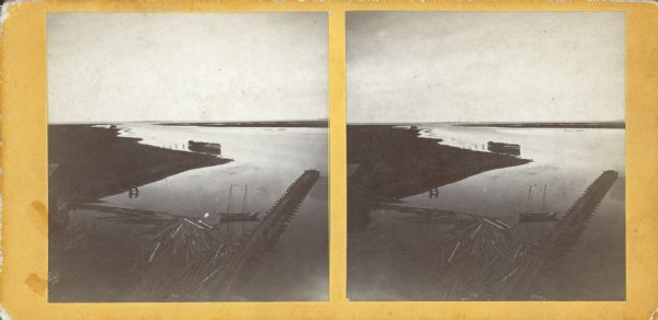 Stereograph of an elevated view looking north from Green Bay. In the foreground logs are floating in the water near boat moored near a pier or jetty. Another boat is near the shoreline in the distance.