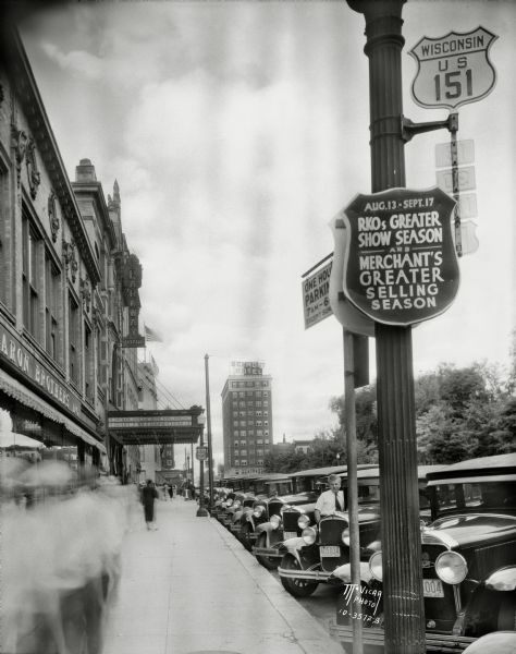 View of the Parkway Theatre marquee down West Mifflin Street, and a sign for the "RKO's Greater Show Season and Merchant's Greater Selling Season" on a lamppost. Included in the view is Baron Brother's department store, 12-18 W. Mifflin Street, and further down the street the Belmont Hotel, 31 N. Pinckney Street.