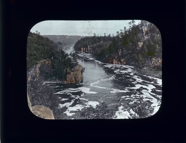 Elevated view looking down at a river. Tall rocky cliffs covered with trees form the shoreline.