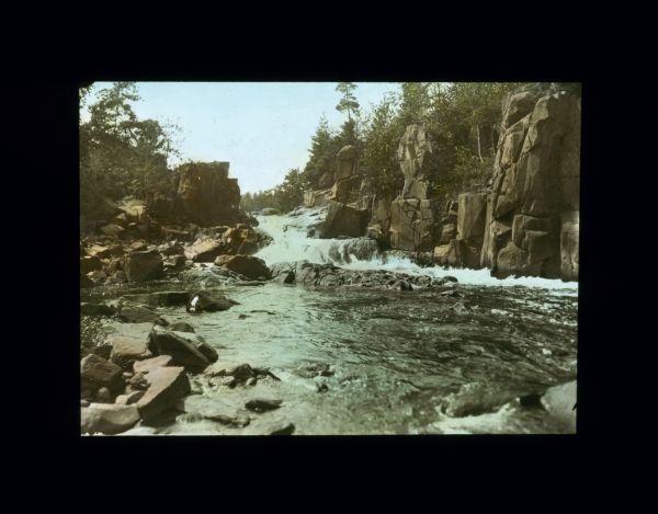 View up center of river with rushing waters, surrounded by rock cliffs.