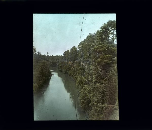 Elevated view of a stream lined by tall trees and water-eroded steep, rocky cliffs.