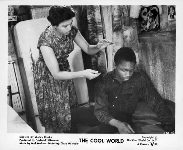 A publicity still from the film "The Cool World" showing Mrs. Custis (Gloria Foster) reaching towards an African American teenage boy who is sitting. A refrigerator is in the background.