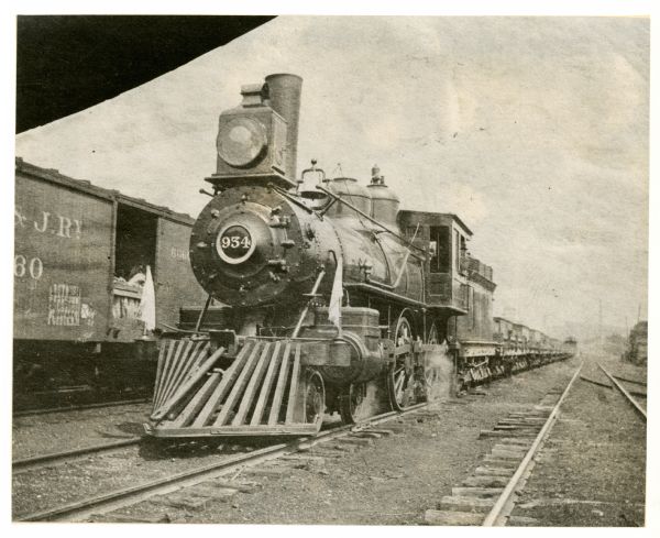 The Chicago, Milwaukee, and St. Paul Railway Engine No. 934, Class H6, sitting on the railroad tracks next to a train car.