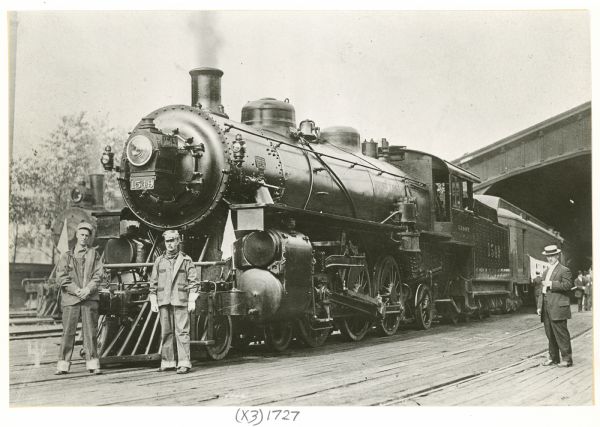 A railroad crew posing with Chicago, Milwaukee, and St. Paul Railway Engine No. 1549 before going to the Guiding Star Picnic at Kansasville, Wisconsin. On the far left is fireman Walter W. Bates. The other two men are unidentified. The location is probably Union Depot in St. Paul, Minnesota.
