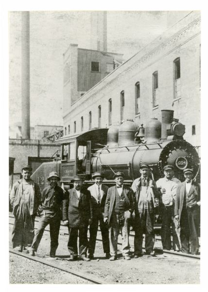 Railroad workers posing in front of locomotive Engine No. 1224 at Stowell Station. From left to right are Fireman John F. Fohey, yardmaster John Rice, Waymaster Harry Sheasby, unidentified, unidentified, engineer Omro B. Mills, Engineer Julius Wellso, and Switchman Joseph Salentine.