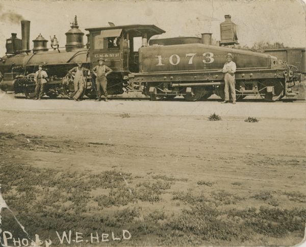Several crew members posing next to the Chicago, Milwaukee, and St. Paul Railway switching Engine No. 1073, which operated in Menasha, Wisconsin.
