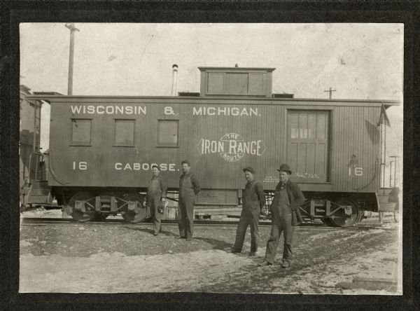 Four men (possibly railroad workers) standing in front of Wisconsin & Michigan Caboose #16.